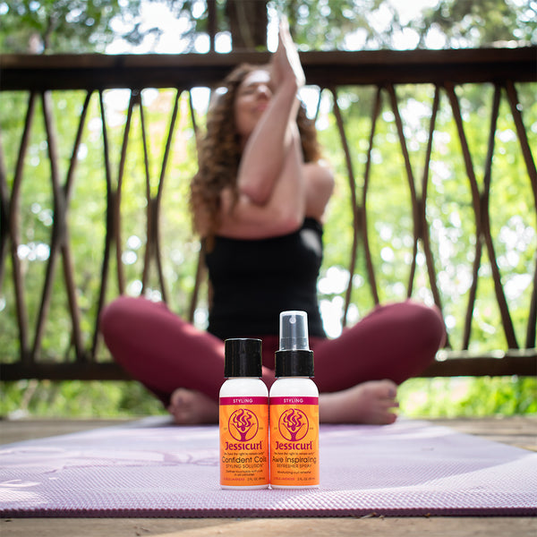 Two bottles of Jessicurl hair care products on a yoga mat with a person practicing yoga in the background.